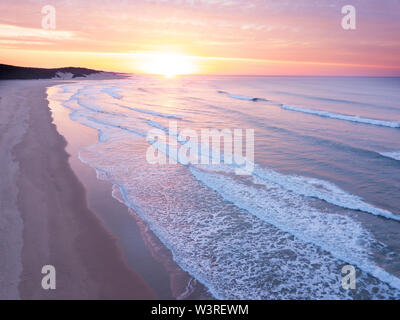 Aerial view over a wide open ocean and beach at sunrise