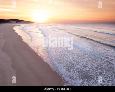 Aerial view over a wide open ocean and beach at sunrise