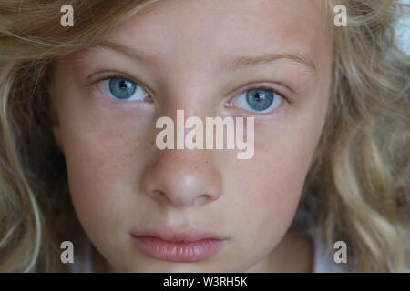 Closeup of a beautiful preteen girl with blue eyes and a sad, serious stare Stock Photo