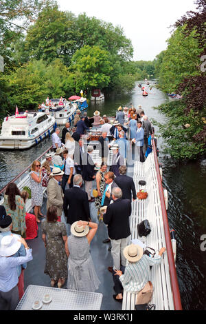 Hurley, Berkshire, UK. 17th July, 2019. Passengers on board the Waterman following the swan uppers as they leave Hurley Lock on day three of Swan Upping 2019. A week long survey of the the swans on the River Thames, from Sunbury in Surrey to Abingdon in Oxfordshire. The Royal Swan Uppers, who wear the scarlet uniform of Her Majesty The Queen, travel in traditional rowing skiffs together with Swan Uppers from the Vintners' and Dyers' livery companies. Credit: Julia Gavin/Alamy Live News Stock Photo