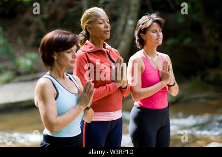 Middle aged women doing yoga beside river Stock Photo