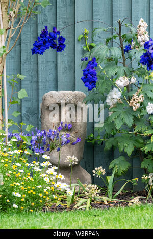 A reconstituted stone garden ornament in the form of one of the famous Easter Island heads sits nestled between flowers in a private garden Stock Photo