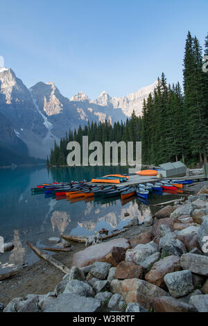 canoes and mountains reflected in calm clear water of Moraine Lake Alberta, Canada Stock Photo