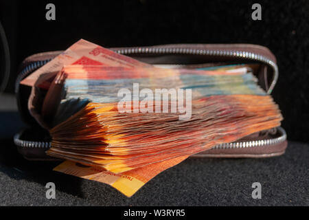 A close up view of pile of two hundred, one hundred and fifty rand sound african notes coming out the front of a brown leather wallet on a isolated ba Stock Photo