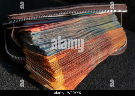 A close up view of pile of two hundred, one hundred and fifty rand sound african notes coming out the front of a brown leather wallet on a isolated ba Stock Photo