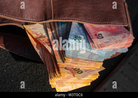 A close up view of pile of two hundred, one hundred and fifty rand sound african notes coming out the front of a brown leather handbag Stock Photo