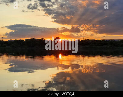 Wonderful sunset over the city horizon with reflection on the calm lake water in a silent summer evening. Stock Photo
