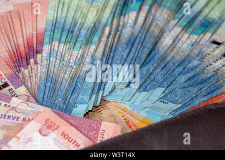 A close up view of pile of two hundred, one hundred and fifty rand sound african notes spread out next to a brown leathe wallet Stock Photo