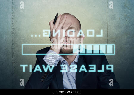 businessman or office worker waits bored and long on his slow computer or internet connection, displaying a loading bar and a message Stock Photo