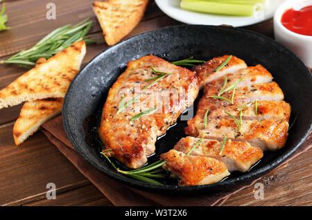 Roasted pork steaks in frying pan, toast and tomatoes sauce on wooden table, close up view Stock Photo