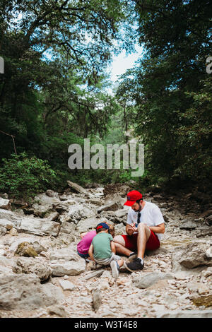 Dad helping daughter and son look for rocks while hiking Stock Photo