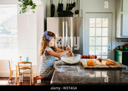 Young girl sitting in kitching mixing peach muffin batter Stock Photo