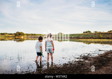 Young boy and girl looking for fish with nets in lake Stock Photo