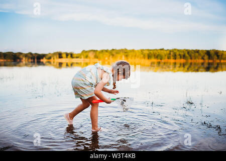 Young girl bending down to see fish in water at the lake Stock Photo