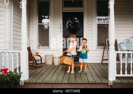 Young girl and boy smiling with basket full of peaches on front porch Stock Photo
