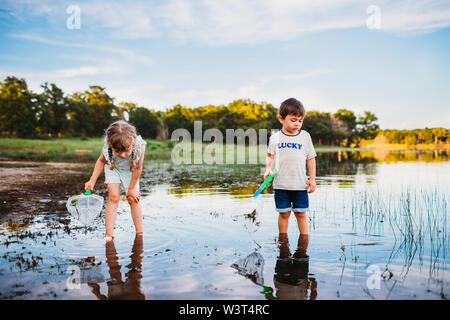 Young girl and boy looking into lake to catch fish with fishing net Stock Photo