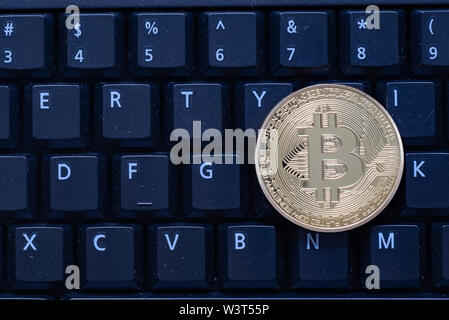 A gold colored bitcoin sitting on a black computer keyboard, symbolic of the cryptocurrency Stock Photo