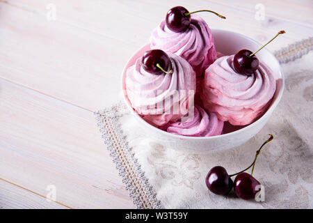 Lots of sweet pink cherry cakes in a white plate on a wooden background. Pink cherry marshmallows. Red cherry Stock Photo