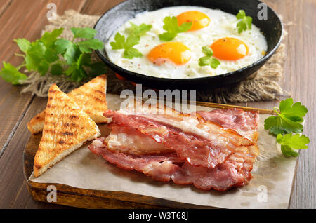Appetizer fried bacon and toasts on cutting board.  Fried eggs on frying pan