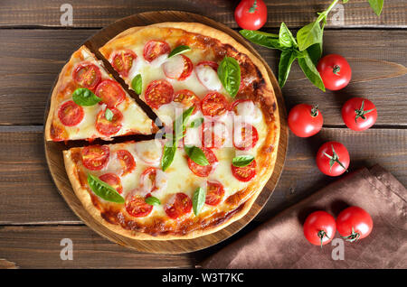 Appetizing pizza Margherita on a cutting board, fresh tomatoes and basil on wooden table. Top view, flat lay Stock Photo