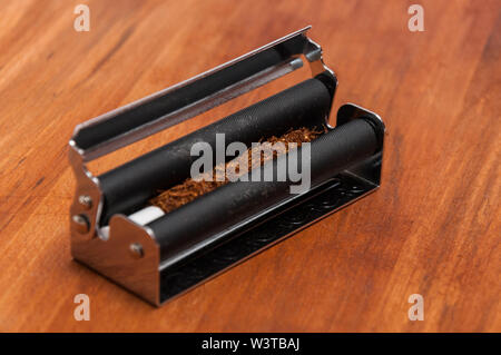 Black machine with hand rolling tobacco with the filter on the wooden background Stock Photo