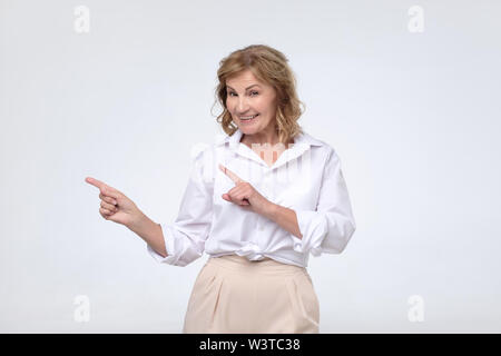 mature woman smiling broadly, pointing fingers away, showing something interesting and exciting Stock Photo