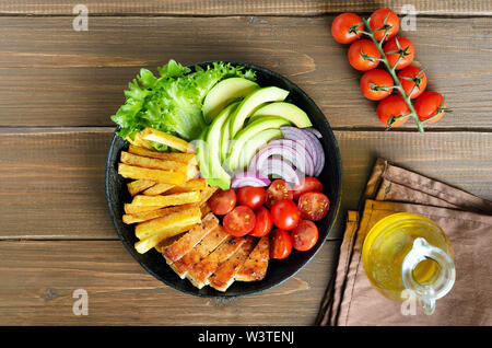 Grilled sliced pork steak with potatoes, tomatoes and avocados in frying pan on wooden table. Top view, flat lay Stock Photo