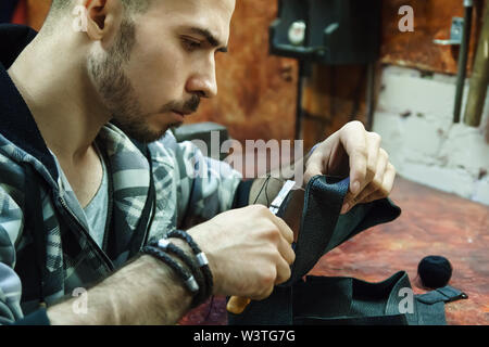 Craftsman intently works with leather. Tanner sews leather goods. Making handmade stuff. Male hands with needle and thread. Man working with needle. Stock Photo