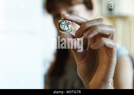 Portrait of woman watchmaker. Girl with blurred face holds clock in hand. Clockwork in fingers. Gears in disassembled watches on blurred background. Stock Photo