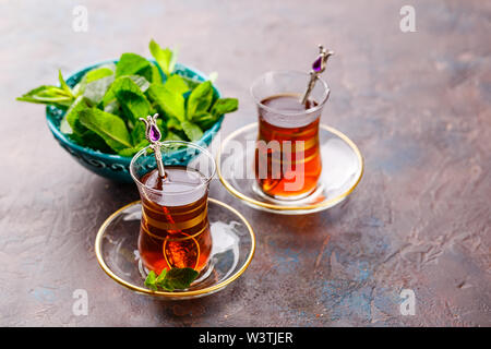 Traditional Turkish black tea in glass at decorative plates with mint on concrete background Stock Photo
