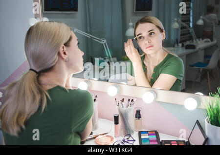Woman correcting eyebrows form. Young pretty woman making make-up near mirror in studio Stock Photo