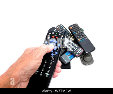 Horizontal close-up shot of a woman’s hand holding a remote control with blue, gray, green, and red buttons.  There is a pile of old remote controls i Stock Photo