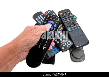 Horizontal close-up shot of a woman’s hand holding a remote control with blue, gray, green, and red buttons.  There is a pile of old remote controls i Stock Photo
