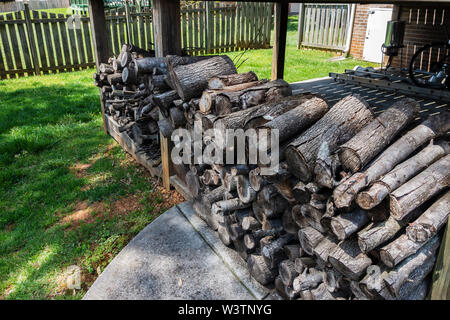 A rack of cut and stacked firewood stored in a yard under an overhang. USA. Stock Photo