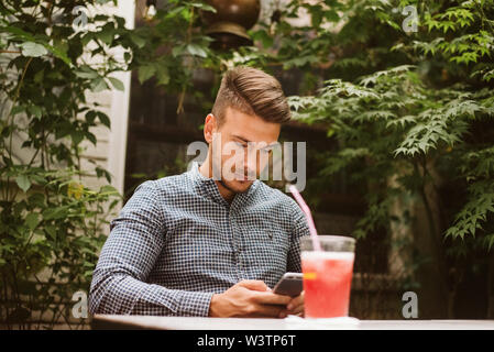 Young man sitting in a cafe, drinking coffee and talking on a mobile phone Stock Photo