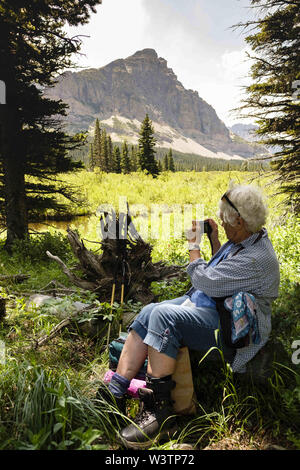 Glacier National Park, Montana, USA. 16th July, 2019. SANDY SMITH of Big Fork, Montana, takes a picture of tree roots while hiking with her women's hiking group on Pitamakan Pass Trail in East Glacier in Glacier National Park. Credit: Kent Meireis/ZUMA Wire/Alamy Live News Stock Photo