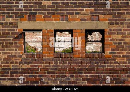 Three empty and broken windows in the brick wall of a disused factory building in Sheffield, UK. Stock Photo