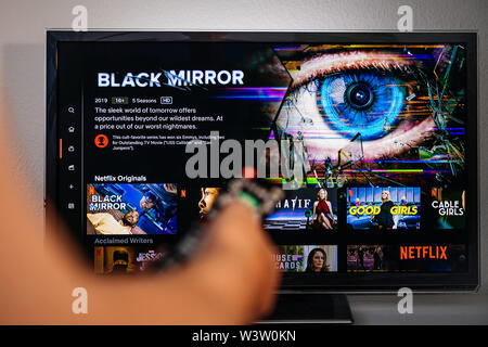 Paris, France - Jul 10, 2019: Senior man hand holding remote control watching the Black Mirror on Netflix - it is a British science fiction anthology television series created by Charlie Brooker, Stock Photo