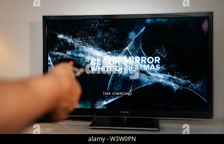 Paris, France - Jul 10, 2019: Senior man hand turning with remote control watching the Black Mirror on Netflix - it is a British science fiction anthology television series created by Charlie Brooker, Stock Photo