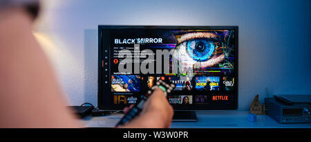 Paris, France - Jul 10, 2019: Senior man hand holding remote control watching the Black Mirror on Netflix - British science fiction television series created by Charlie Brooker selecting episode Stock Photo