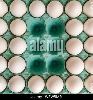 White eggs arranged together in a green egg carton with empty spaces in the middle. Stock Photo