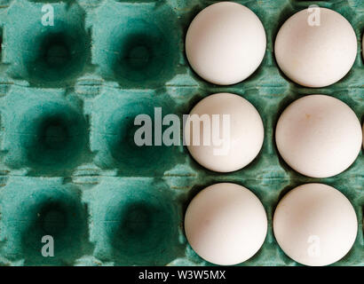 white eggs arranged together to the right side of a green egg carton with empty spaces on the left side. Stock Photo