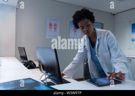 Female doctor using digital tablet while working on computer at desk Stock Photo