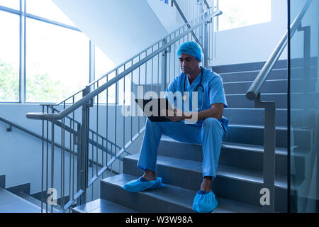 Male surgeon writing on clipboard while sitting on the stairs of hospital Stock Photo