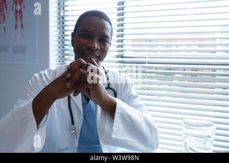 Male doctor sitting with hands clasped in the hospital Stock Photo