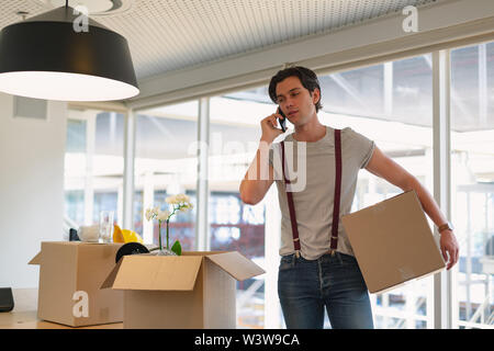Male executive talking on mobile phone while holding a cardboard box in the conference room Stock Photo