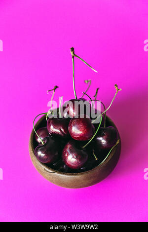 Fresh cherries in a small bowl on a bright pink background, top view - Image Stock Photo