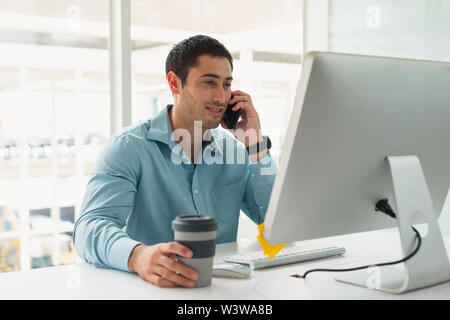 Male executive talking on mobile phone while working on computer at desk Stock Photo