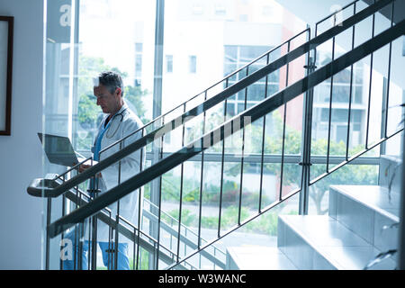Male doctor using laptop while walking the stairs Stock Photo