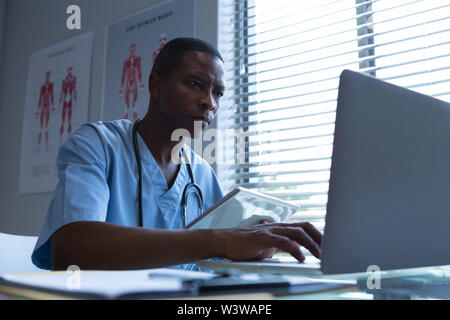 Male surgeon using laptop while holding digital tablet at desk Stock Photo